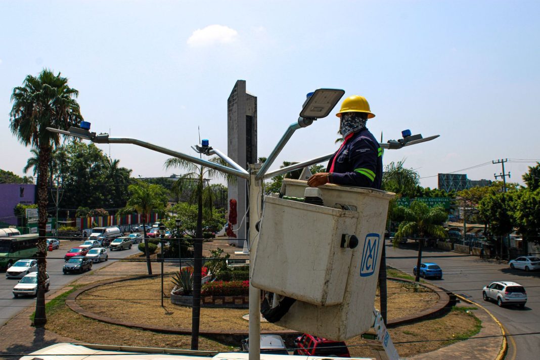 Trabajadores municipales realizan la instalación de nuevas luminarias en el camellón de una avenida principal.